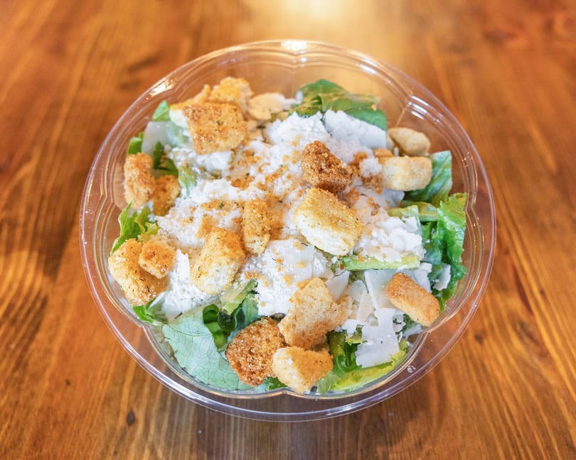 Caesar salad with romaine lettuce, croutons, and parmesan cheese in a clear plastic container.