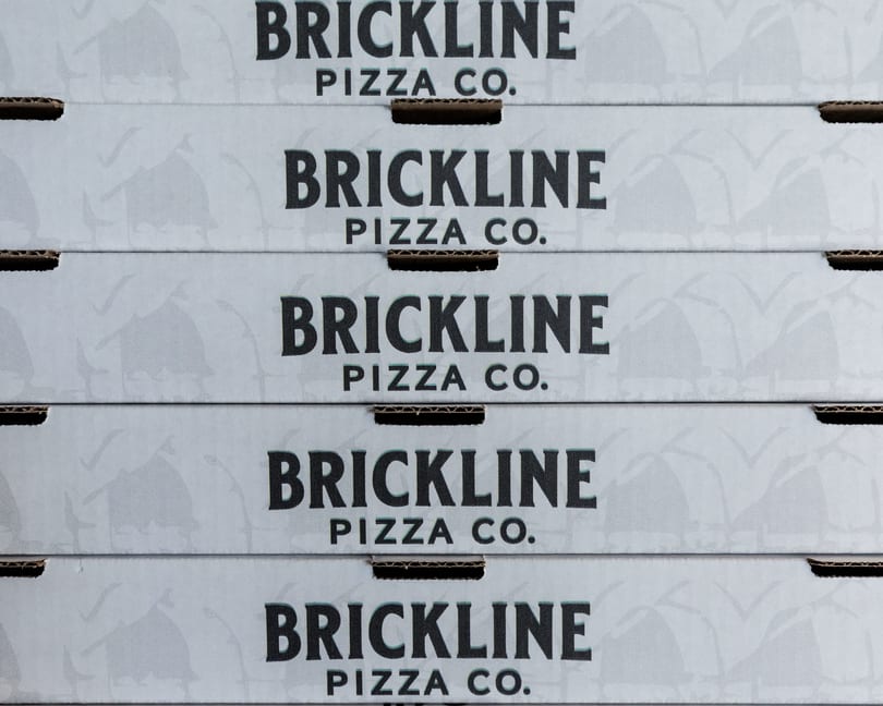 A stack of five white Brickline Pizza Co. pizza boxes with black lettering.