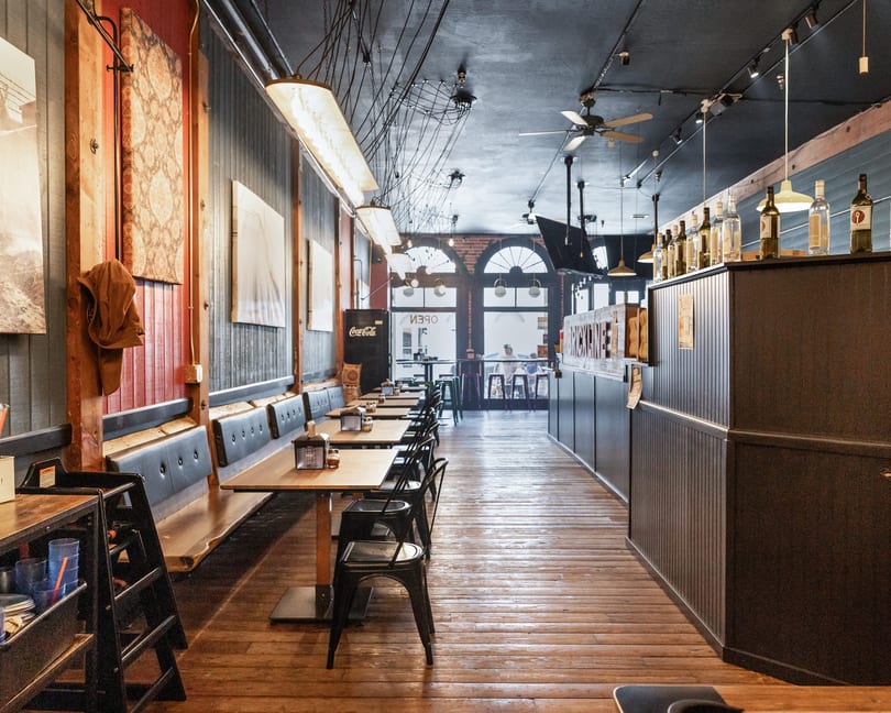 Long, narrow restaurant interior with wooden floors, booth seating, and arched windows at the far end.